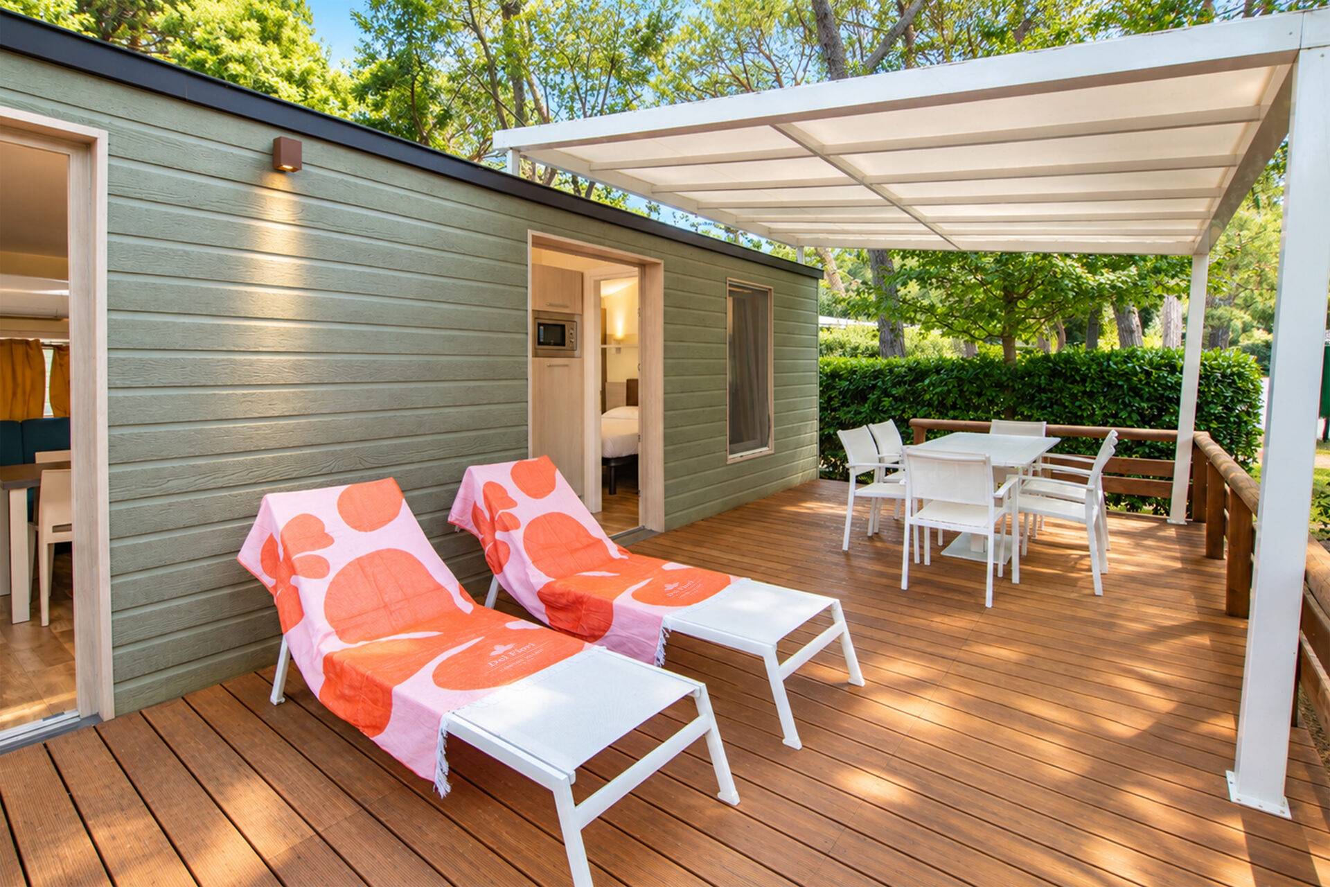Terrazza in legno dello Chalet Natura Four Beds con due lettini prendisole, tavolo da pranzo e pergola bianca.