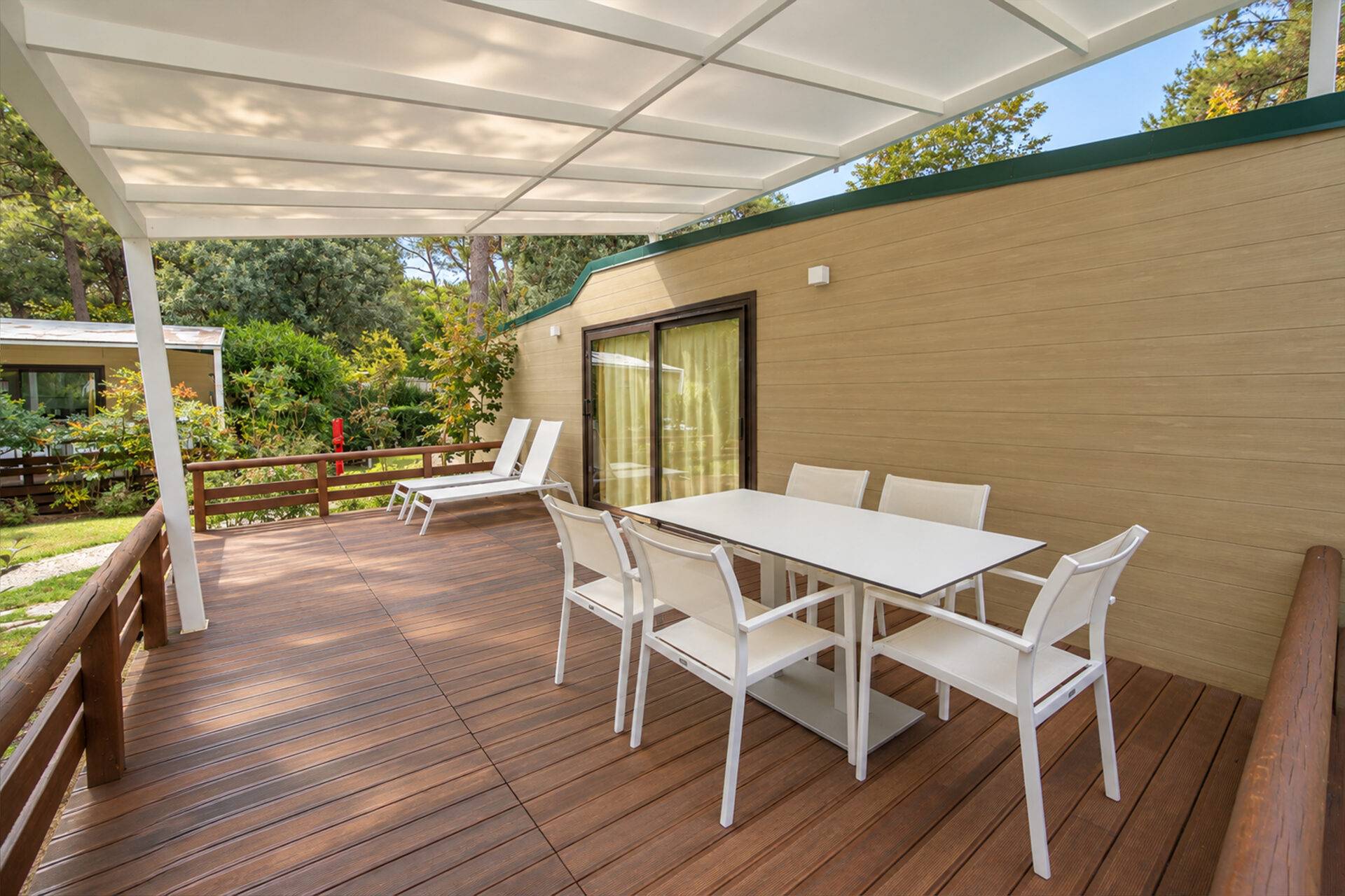Terrazza coperta dello Chalet Natura Family al Camping Dei Fiori con tavolo, sei sedie e due lettini prendisole.