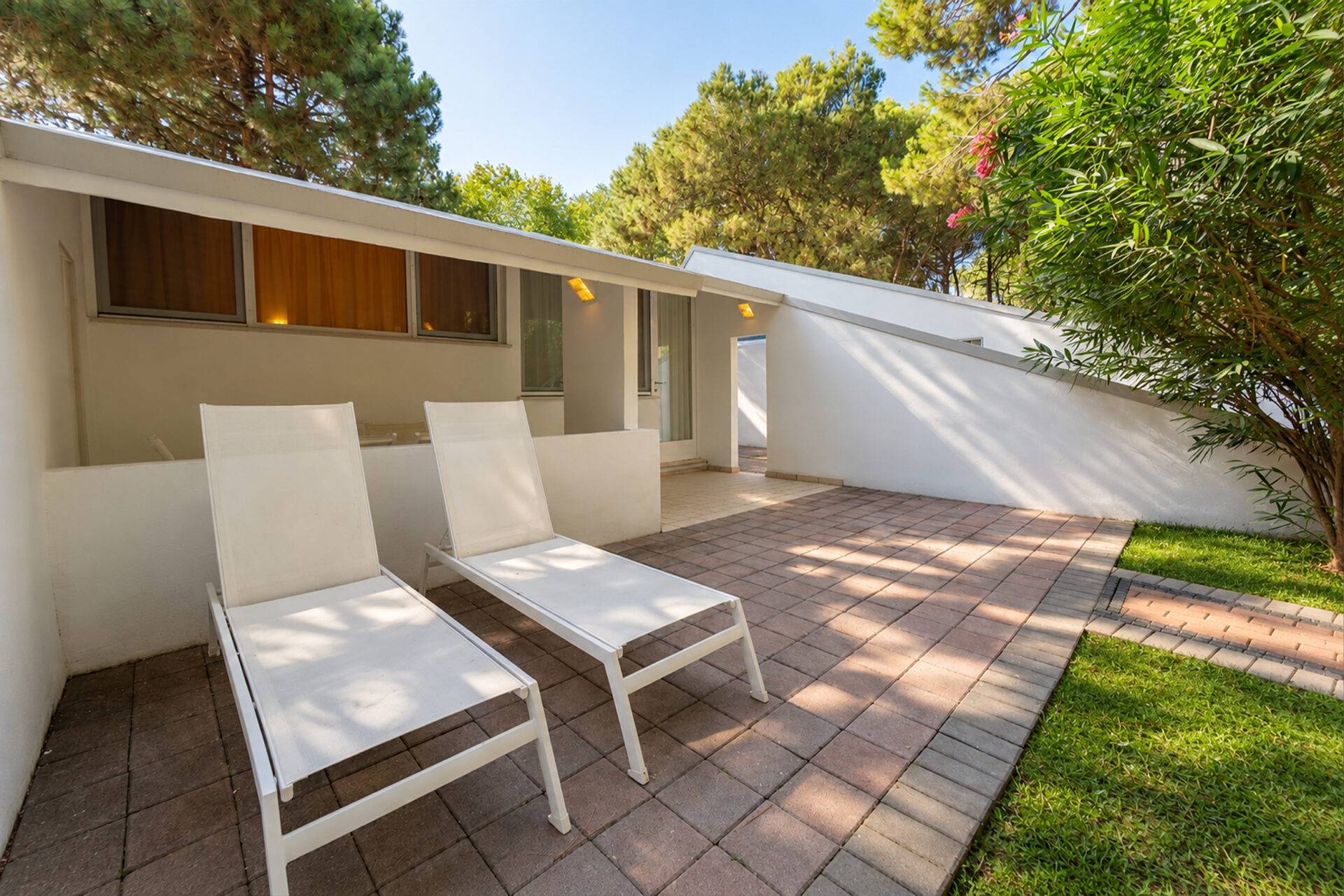 Terrasse des Bungalow Garden im Camping Village Dei Fiori mit zwei Sonnenliegen, Ziegelpflaster und Garten.