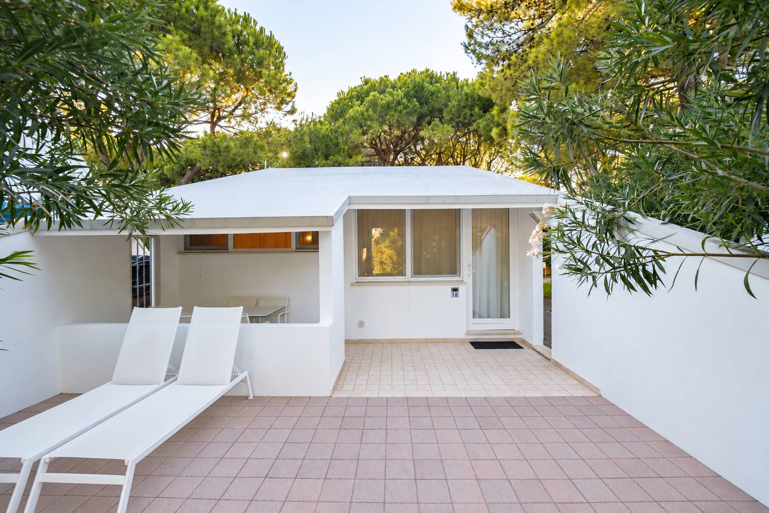 Esterno del Bungalow Mare al Camping Dei Fiori con terrazza pavimentata, lettini e verde circostante.