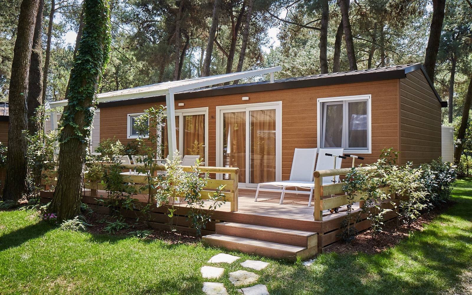 Veranda in legno dello Chalet Natura Superior con lettino prendisole, pergola bianca e giardino nella pineta.