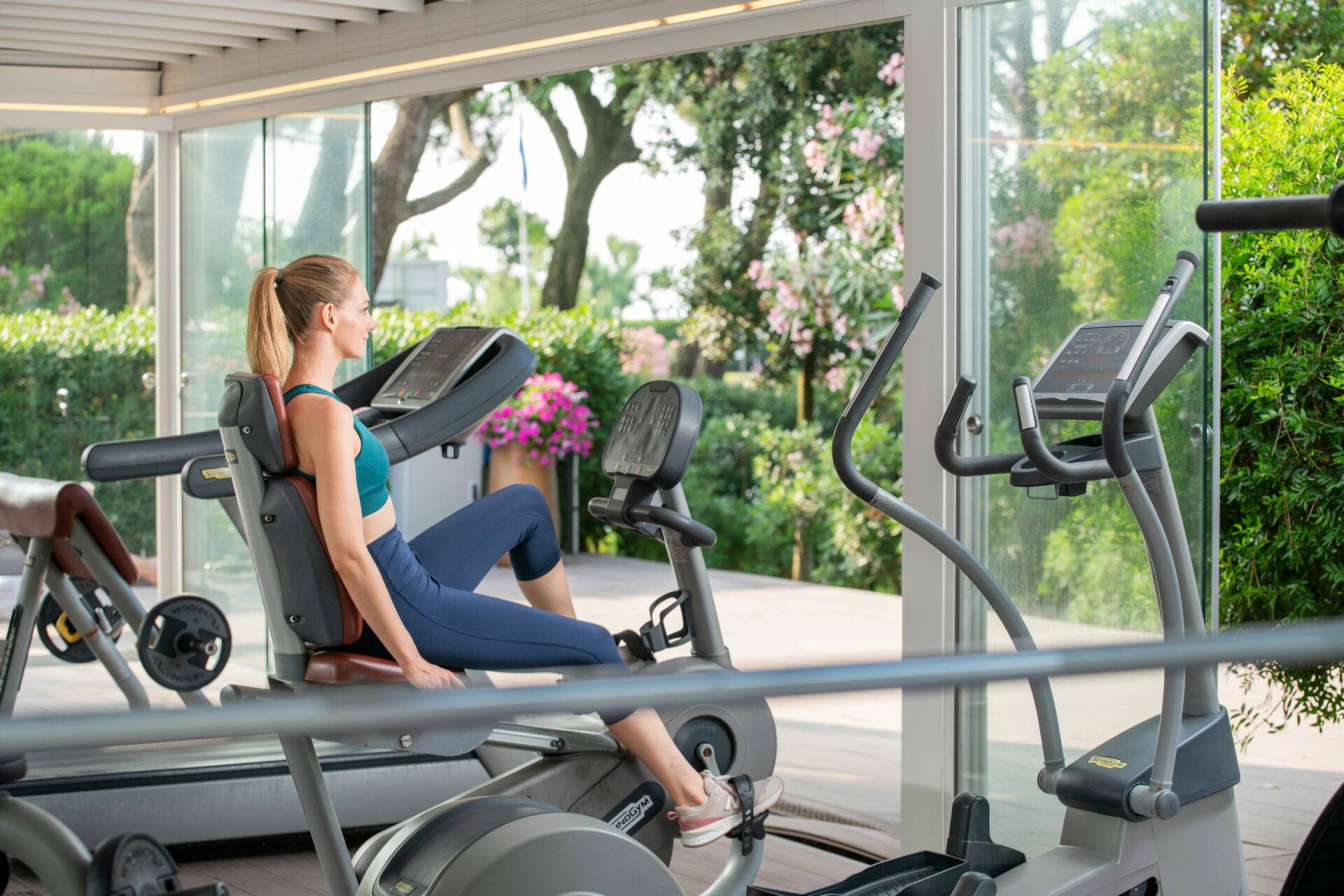 Ospite si allena sulla cyclette nella palestra del Camping Village Dei Fiori con vista sul giardino.