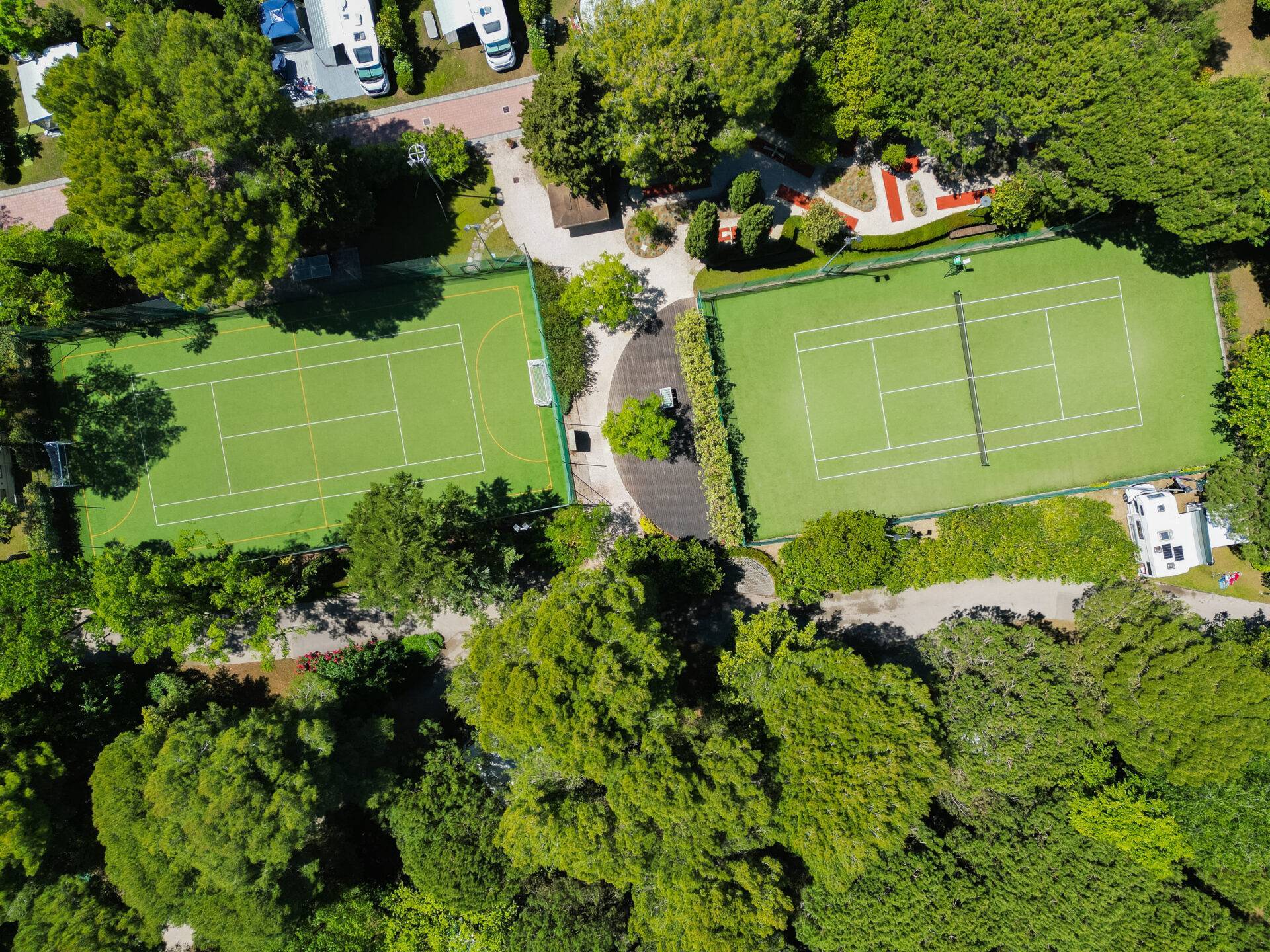 Vista aerea del campo da tennis e del campo polivalente per calcetto e basket del Camping Village Dei Fiori, tra gli alberi.