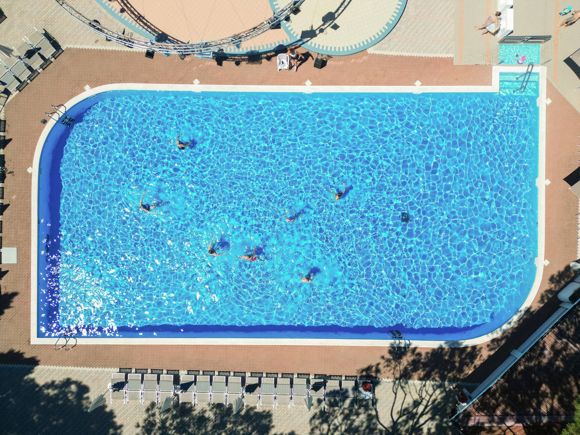 Vista aerea della piscina per adulti del Camping Dei Fiori, con ospiti che nuotano e lettini lungo il bordo.
