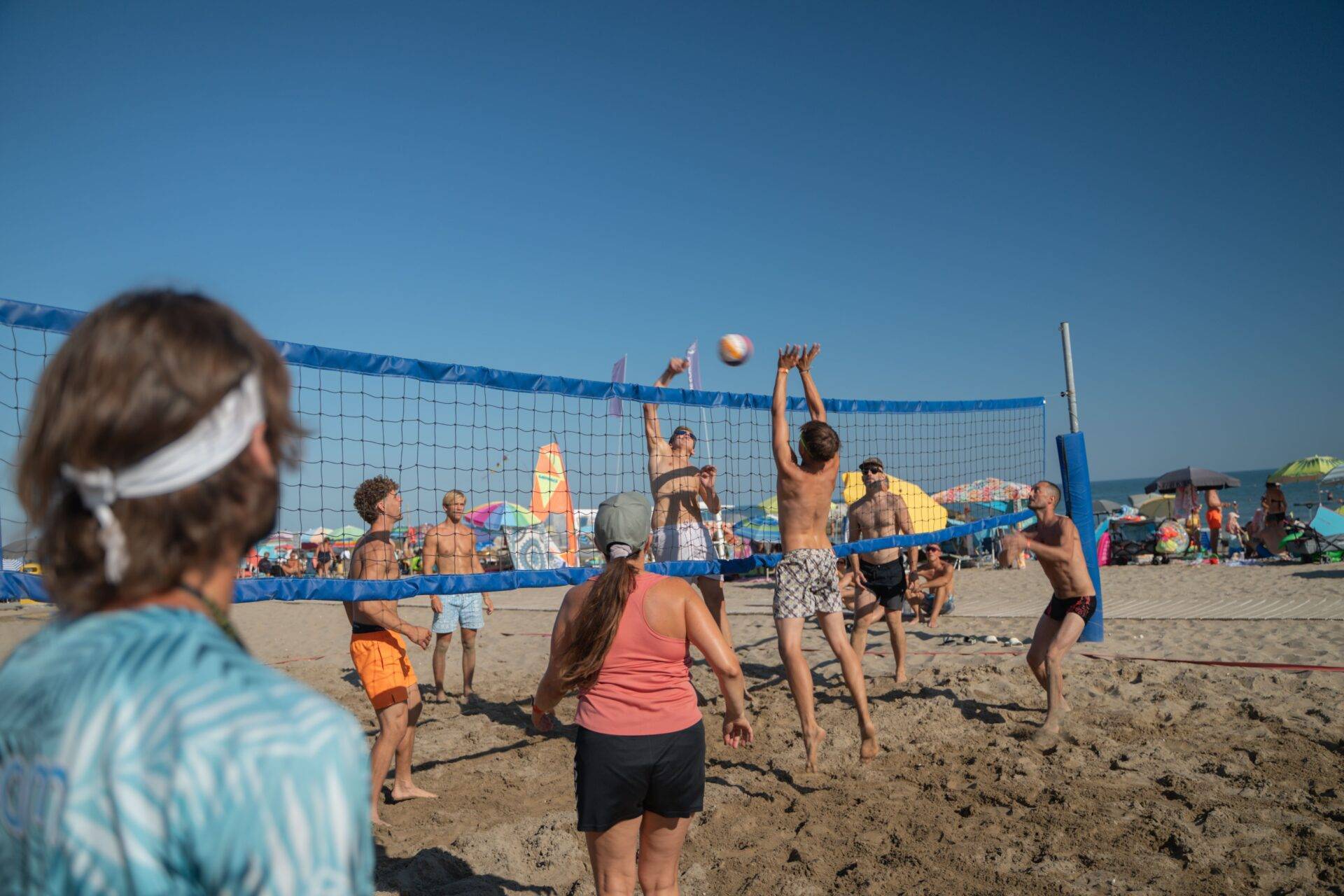 Ospiti giocano a beach volley sulla spiaggia del Camping Village Dei Fiori, tra sabbia, ombrelloni e mare.