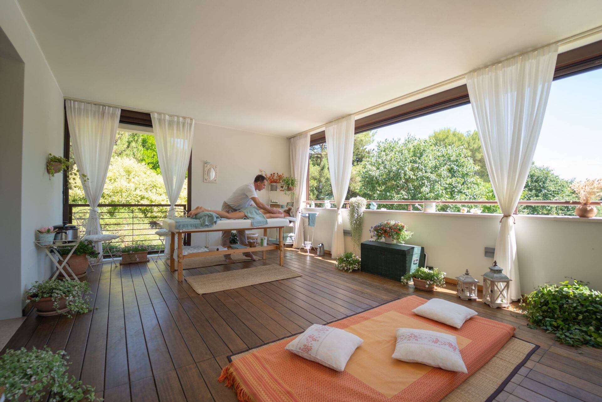 Vista della terrazza wellness del Camping Village Dei Fiori con un massaggio in corso, materassino, cuscini e piante.