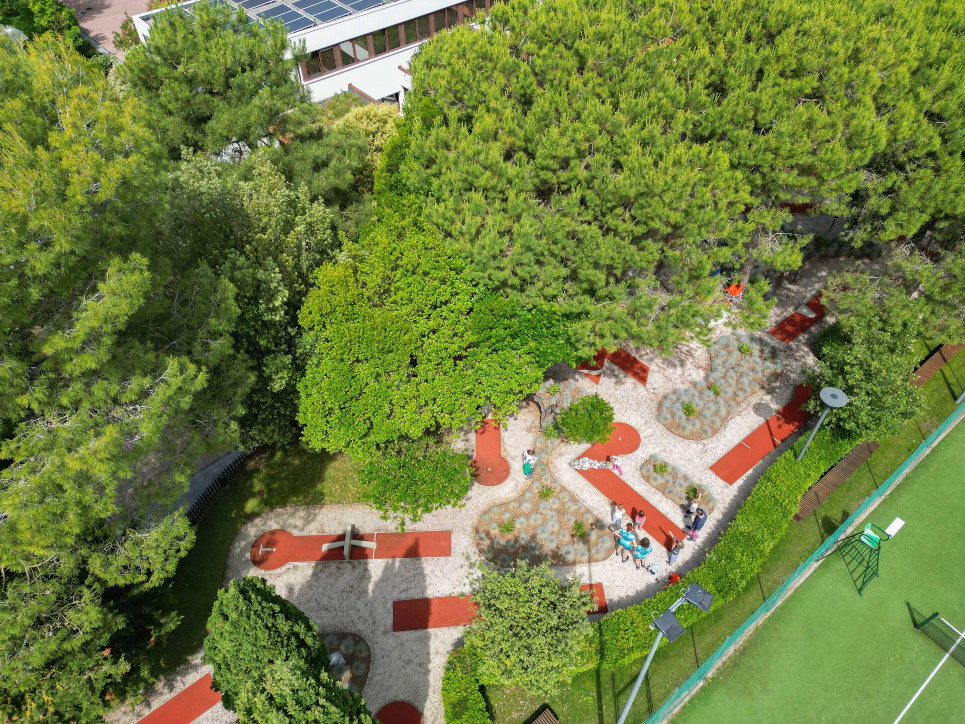Vista dall'alto del percorso di minigolf tra alberi e aiuole, con bambini e adulti al Camping Village Dei Fiori.