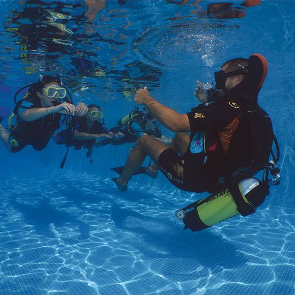Istruttore di diving mostra un gesto con la mano a due partecipanti durante una lezione subacquea nella piscina del Camping Mediterraneo.