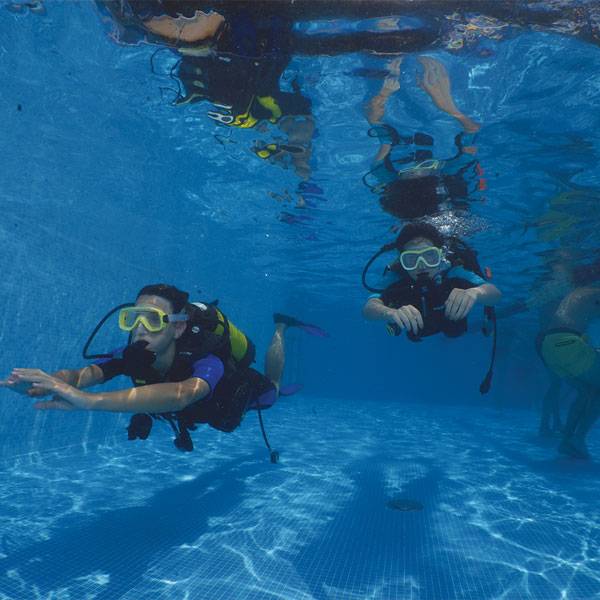Due partecipanti a un corso di diving nuotano sott'acqua con maschere, pinne e bombole nella piscina del Camping Mediterraneo.