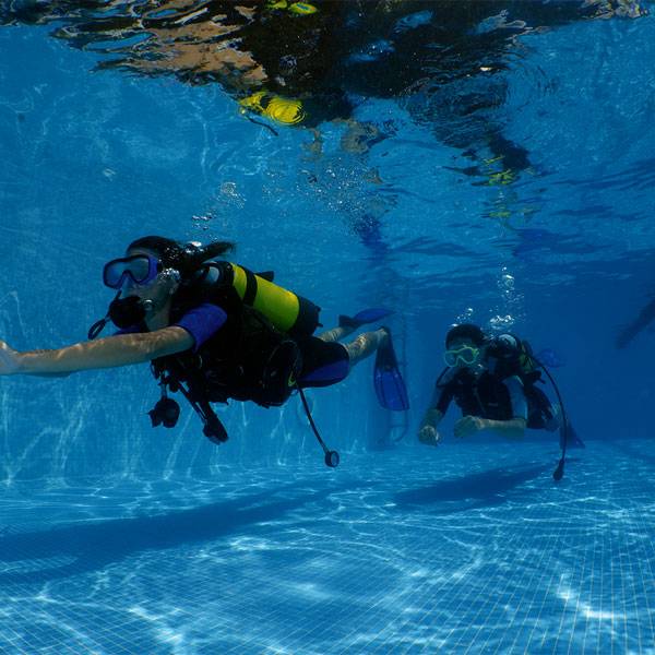 Due subacquei con bombole, maschere e pinne si esercitano nuotando sott'acqua nella piscina del Camping Village Mediterraneo.