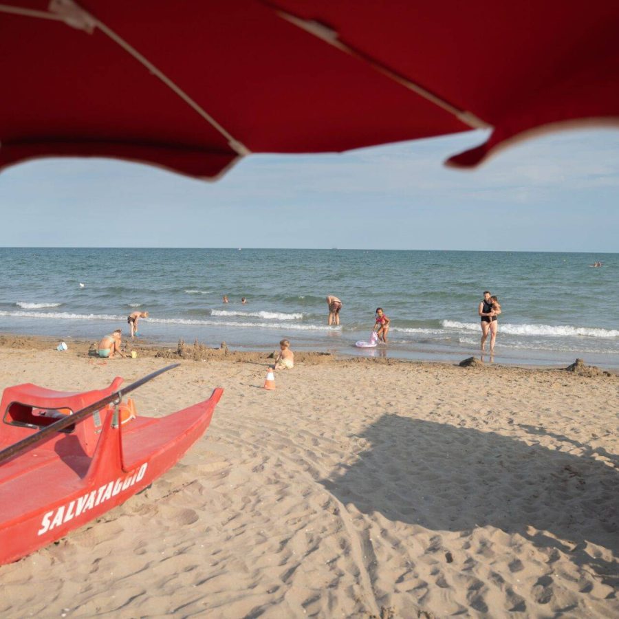 Bambini giocano sulla sabbia e famiglie si rilassano vicino al mare sulla spiaggia del Camping Village Dei Fiori.